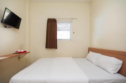 a bedroom with a white bed and a television at AVA Guesthouse Mitra RedDoorz Lampung in Bandar Lampung