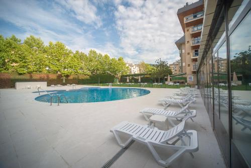 een zwembad met witte ligstoelen naast een gebouw bij Oroel Hotel & SPA in Jaca