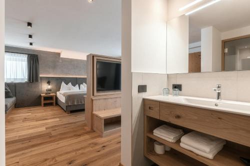 un bagno con lavandino e una camera con letto di Hotel Niblea Dolomites a Ortisei