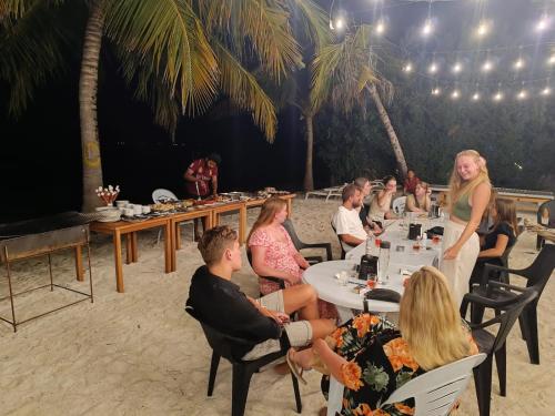 un gruppo di persone seduti ai tavoli sulla spiaggia di The Sunset Villa a Dhiffushi