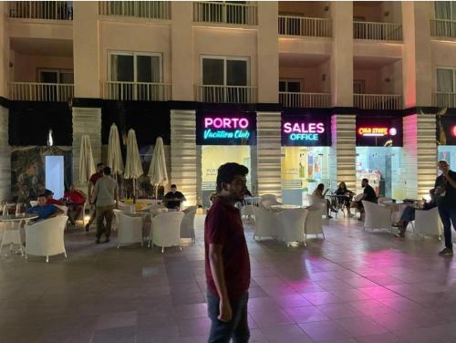 a man walking through a mall with tables and chairs at تمتع بالإقامة في شاليه فندقي بمنتجع جولف بورتو مارينا الساحل الشمالي - Enjoy your stay at Golf Porto Marina Resort El Alamein - North Cost in El Alamein