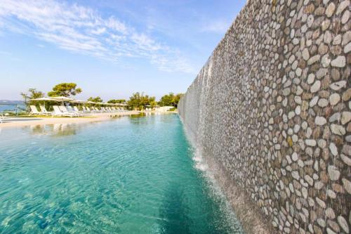 a stone wall next to a beach next to a body of water at SEA HOUSE pool & jacuzzi, bikes, SUP - PRIVILEGE POINT camping & villas in Selce