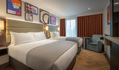 um quarto de hotel com duas camas e uma cadeira em Maldron Hotel Finsbury Park, London em Londres
