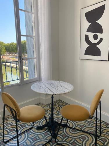 une table et deux chaises dans une pièce avec une fenêtre dans l'établissement Maison d’hôtes Le 1853, à Narbonne