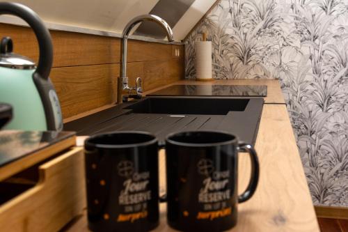 zwei schwarze Kaffeetassen auf einer Küchentheke in der Unterkunft Loft de la raquette in Mons