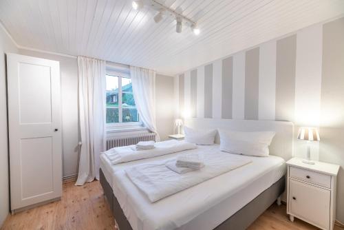 a white bedroom with a large white bed and a window at Landhaus am Meer - Whg 4 Rungholtsand in Utersum