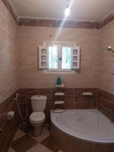 een badkamer met een toilet, een bad en een raam bij فيلا انور يسن ابو كليلة in Zāwiyat al Habbābīyah