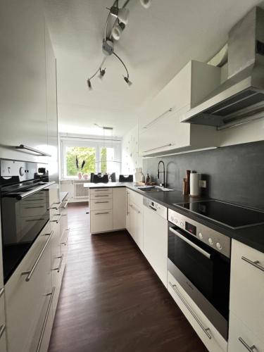 a large kitchen with white cabinets and black appliances at Steinach Apartment in Neuffen