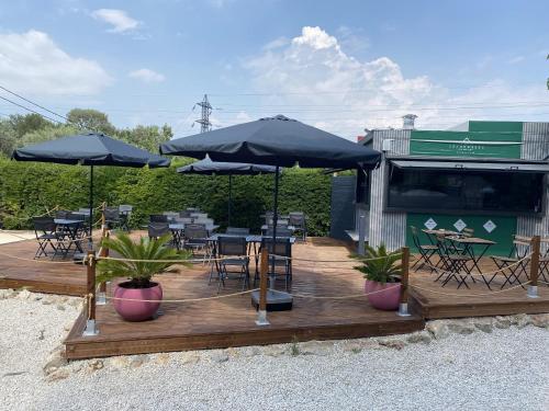 una terraza de madera con mesas, sillas y sombrillas en Hôtel des Moulins, en Allauch