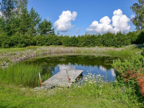 a small pond with a wooden dock in a field at Holiday Home Kannelpirtti 1 by Interhome in Puromäki
