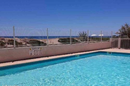 une piscine avec l'océan en arrière-plan dans l'établissement Résidence Tahiti Beach Appart bord de mer, piscine à frontignan plage, à Frontignan