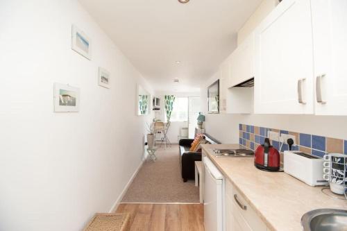 a kitchen with white cabinets and a living room at Seashell - annex in Selsey