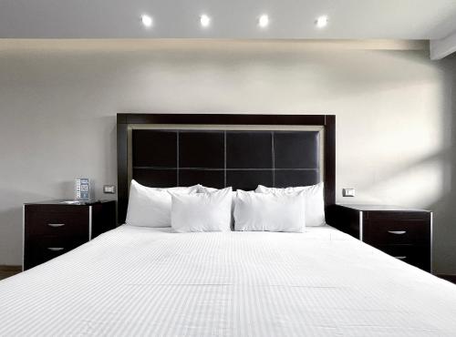 1 dormitorio con 1 cama grande con sábanas y almohadas blancas en Quinta Dorada Hotel & Suites en Saltillo