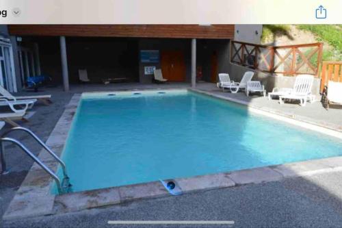 une grande piscine bleue avec des chaises sur la terrasse dans l'établissement Appartement 2 pièces 30 m2 dans résidence de tourisme à LA FOUX D'ALLOS, à La Foux