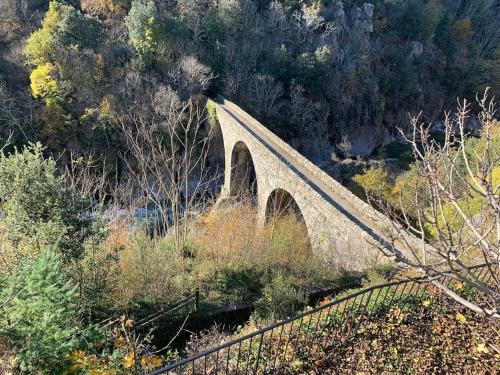 a bridge with two arches on a hill with trees at Villa La source & SPA in Pont-de-Labeaume
