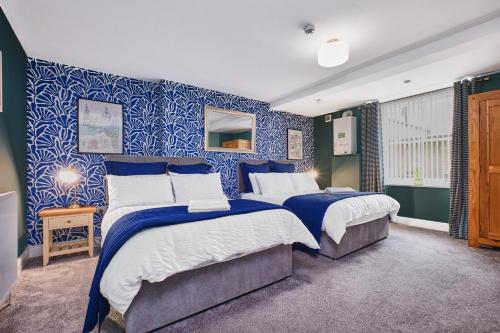 two beds in a bedroom with blue and white wallpaper at Crawford Square Apartment in Derry Londonderry