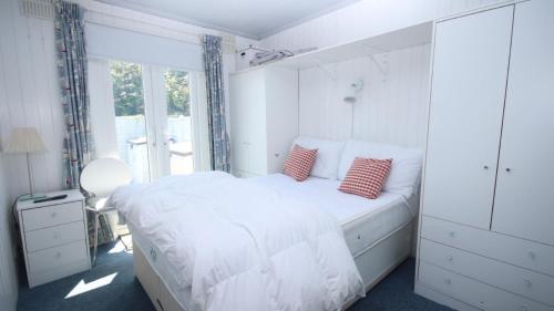 a white bedroom with a white bed with red pillows at 17H Medmerry Park 2 Bedroom Chalet in Earnley