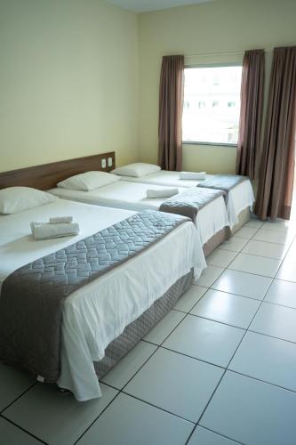 two beds in a hotel room with a window at Pousada Aeroporto in Parnaíba
