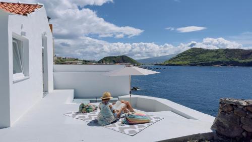 two people sitting under an umbrella on a balcony next to the water at Cliff House, Azores splendid Ocean View in Horta