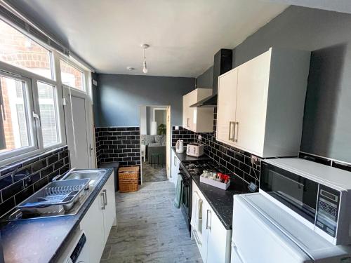 a kitchen with white cabinets and black tile walls at Perfect for Contractors & Families! 7 Beds Free Parking in Birmingham