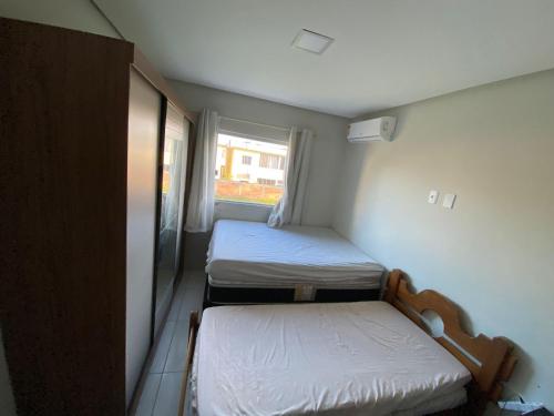 Cette petite chambre comprend 2 lits et une fenêtre. dans l'établissement Apartamento 2 quartos a 300m da Praia, à Santa Cruz Cabrália