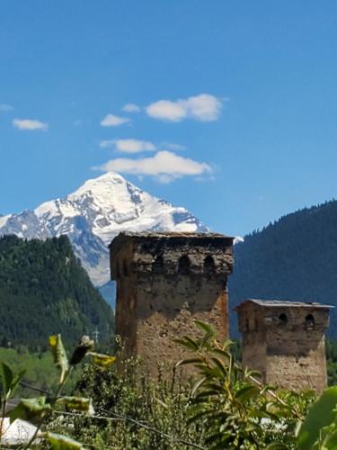 a snow covered mountain in the distance with a building and a tower at Ailama Guesthouse in Mestia