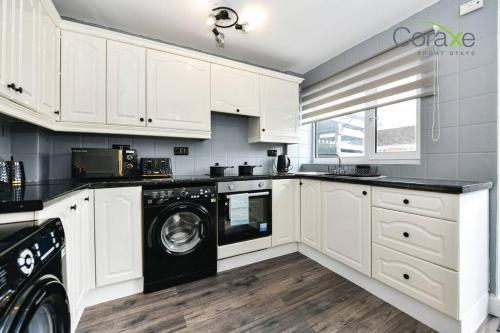 a kitchen with white cabinets and a washer and dryer at 3 Bedrooms Urban Oasis for Contractors and Families by Coraxe Short Stays in Oldbury