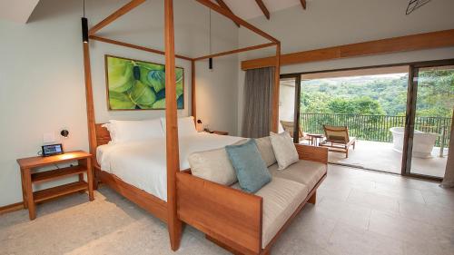 a bedroom with a canopy bed with a couch and a balcony at Tabacón Thermal Resort & Spa in Fortuna