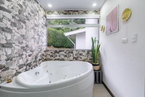 La salle de bains est pourvue d'une baignoire blanche et d'une fenêtre. dans l'établissement House of Turri Suite, Views & Jacuzzi, à Verbena Norte