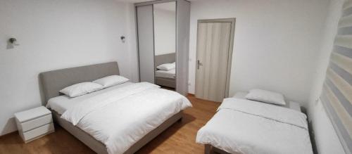 a white bedroom with two beds and a mirror at Apartman Vera in Užice