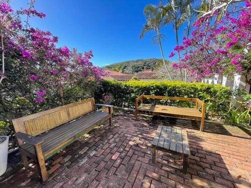 Zwei Holzbänke stehen auf einer mit Blumen bewachsenen Backsteinterrasse. in der Unterkunft Casa em condomínio a 50mt da praia dos ossos in Búzios