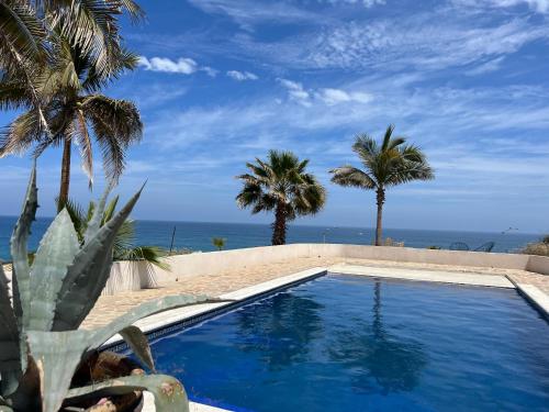 a swimming pool with palm trees and the ocean at Estudio Con Alberca in San José del Cabo