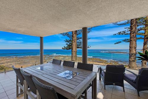a table and chairs on a patio with a view of the ocean at Ocean Pines Apartment 5 in The Entrance