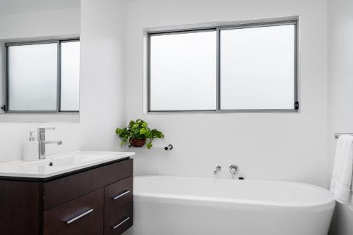 a bathroom with a tub and a sink and two windows at Byron Bay Holiday Homes - Marie and Fred's Villa in Byron Bay
