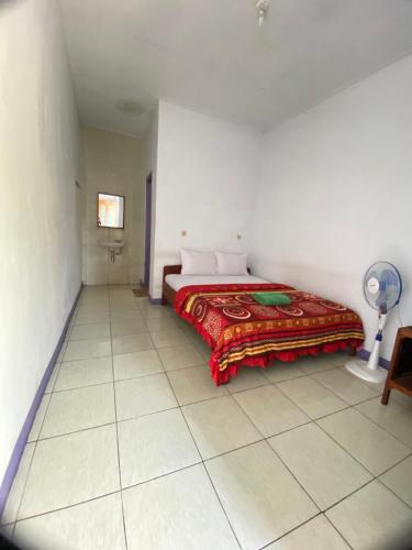 a bedroom with a bed with a red blanket and a fan at Mahoni Guest House in Kelimutu