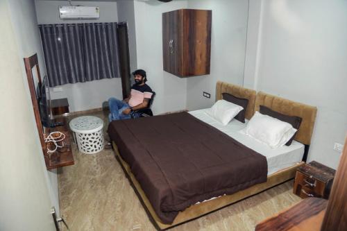 a man sitting in a bedroom with a large bed at Hotel Kiwi Inn in Indore