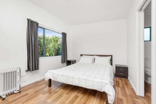a white bedroom with a bed and a window at Seascape Cottage - Mahinepua Bay Clifftop Retreat in Mahinepua