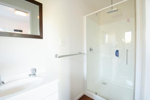 a white bathroom with a shower and a sink at Seascape Cottage - Mahinepua Bay Clifftop Retreat in Mahinepua