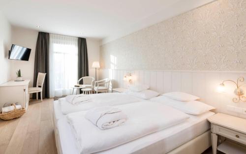a white bedroom with two white beds and a table at Hotel Villa Kastelruth in Castelrotto