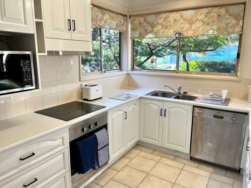 a kitchen with white cabinets and a sink and two windows at Villa Asteri, Hawk's Nest: Walk to everything! in Hawks Nest