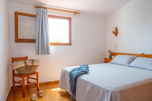 a bedroom with a bed and a window and a chair at Apartamentos Sa Caleta in Sa Caleta