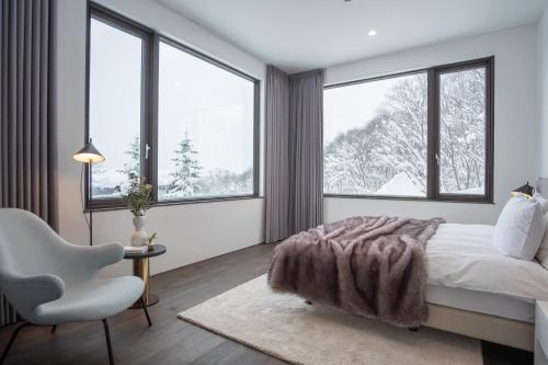a bedroom with a bed and a chair and windows at Song Saa Chalet in Niseko