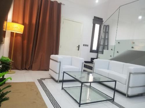 uma sala de estar com duas cadeiras brancas e uma mesa de vidro em Amazing One-Bedroom Villa TownHouse no Dubai