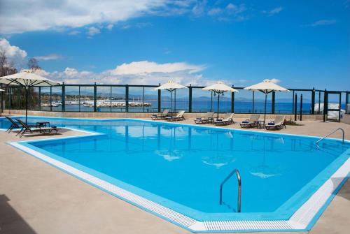 ein großer blauer Pool mit Stühlen und Sonnenschirmen in der Unterkunft Ramada by Wyndham , Athens Club Attica Riviera in Mati