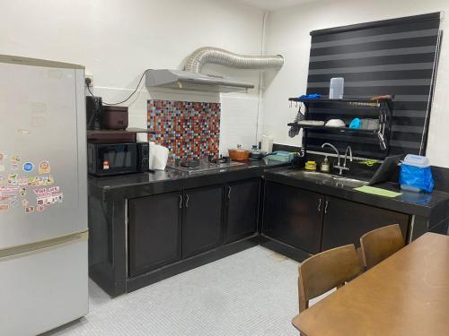 a kitchen with black cabinets and a refrigerator and a table at Hs Homestay Cenderawasih Kuantan Town (5 Bed) in Kuantan