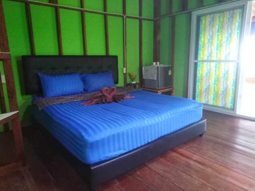 a bedroom with a large bed with blue pillows and green walls at Koh Mook Rem Ley in Trang