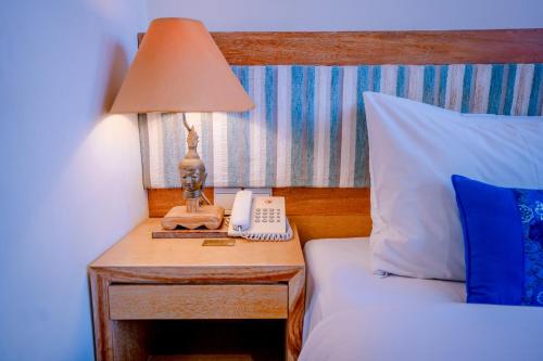 a bed with a table with a lamp and a phone at Pondok Sari Kuta in Kuta