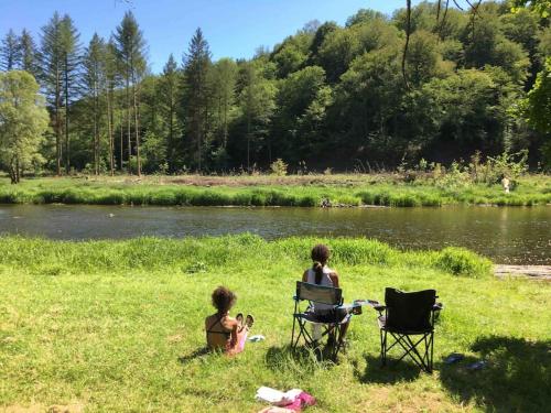 two people sitting in chairs in the grass near a river at La Casa Kemtio in Nollevaux