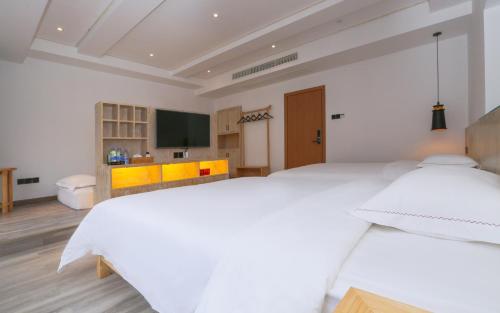 a white bedroom with two beds and a tv at Cozy Boutique Hotel in Zhangjiajie