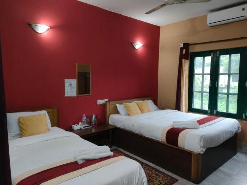 2 Betten in einem Zimmer mit roten Wänden in der Unterkunft Wild Horizons Guest House in Sauraha